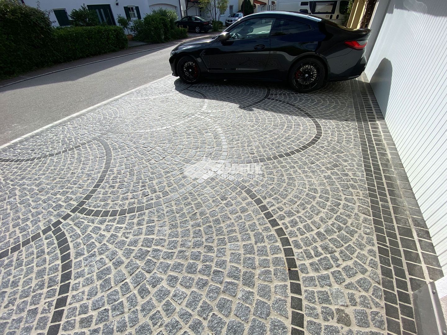 Ein schwarzes Auto ist auf der Einfahrt abgestellt, neben einem eleganten Pflasterweg aus Steinen.