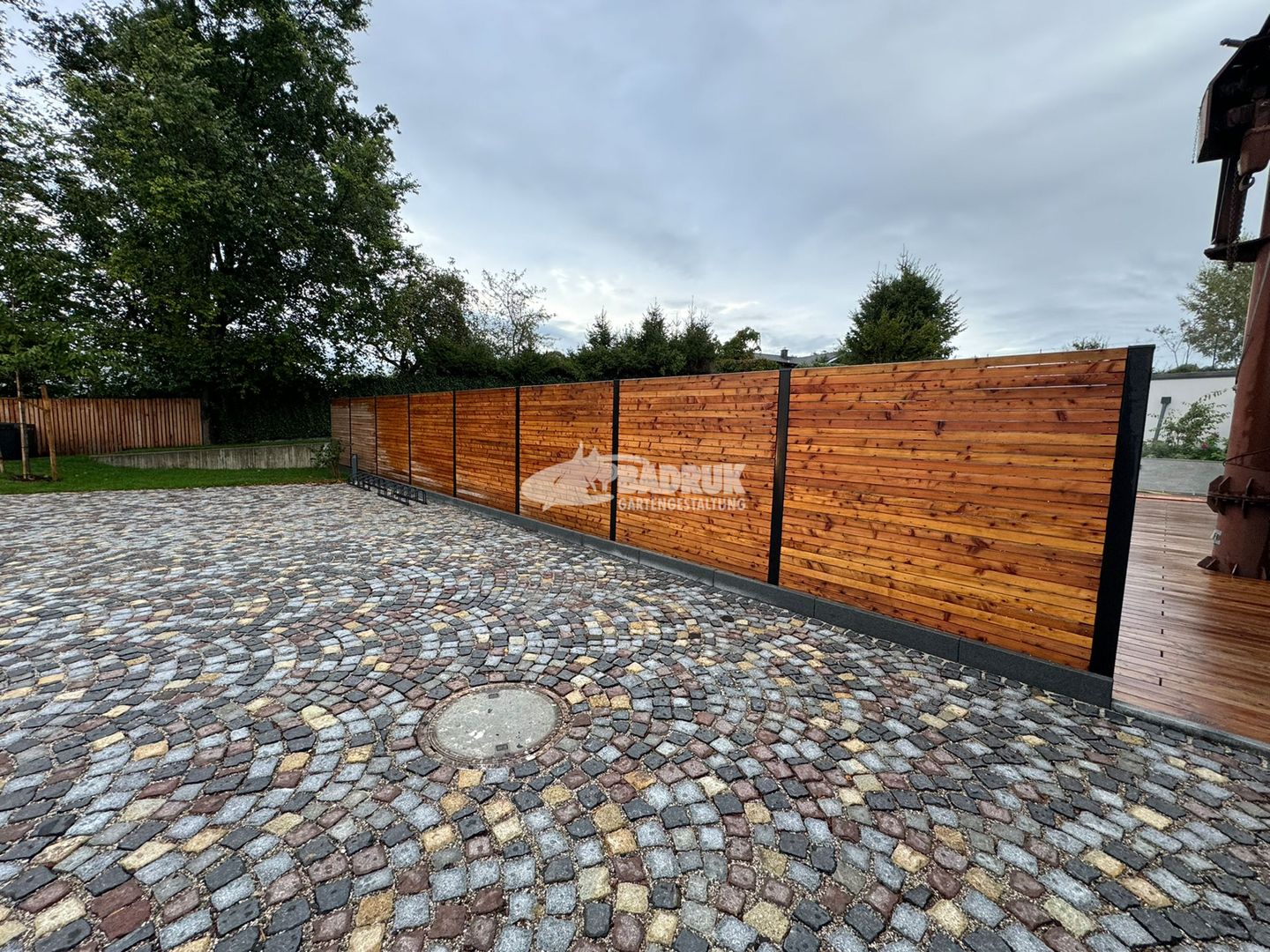 Ein einladender Holzzaun umgibt einen Steinweg und eine Backsteinpatio, perfekt für stilvolle Pflasterarbeiten.