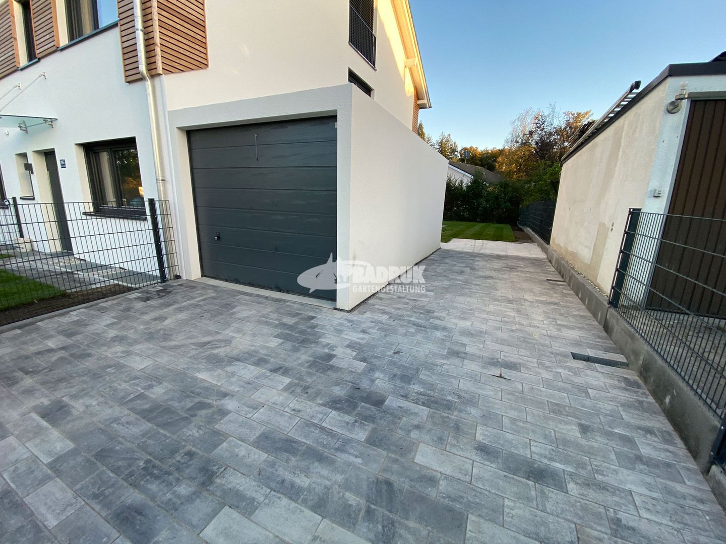 Auffahrt mit Garage und Zaun, umgeben von neuem Pflaster.